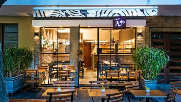 An outdoor seating area with tables and chairs, a sign reading "Togu", and potted plants. - Studio Bartho Leblon (Leblon Rio de Janeiro)