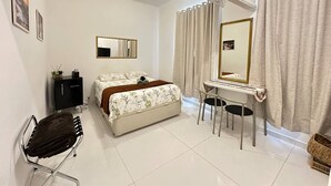 A bedroom with a bed, a desk, two chairs, a mirror, and a wardrobe. - Studio Bartho Leblon (Leblon Rio de Janeiro)