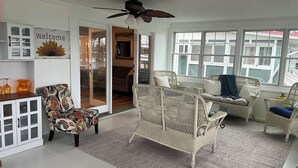 A spacious room with wicker furniture, a ceiling fan, and large windows. - Chautauqua Lake Front Property - Short Walk to the Village of Bemus Point! (Bemus Point)