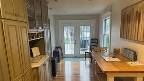A kitchen with wooden cabinets, a dining table, and a view through the glass doors. - Chautauqua Lake Front Property - Short Walk to the Village of Bemus Point! (Bemus Point)