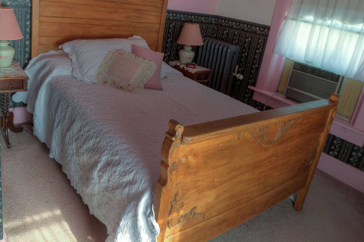 A bedroom with a wooden bed, a nightstand with a lamp, a radiator, and a window with curtains.