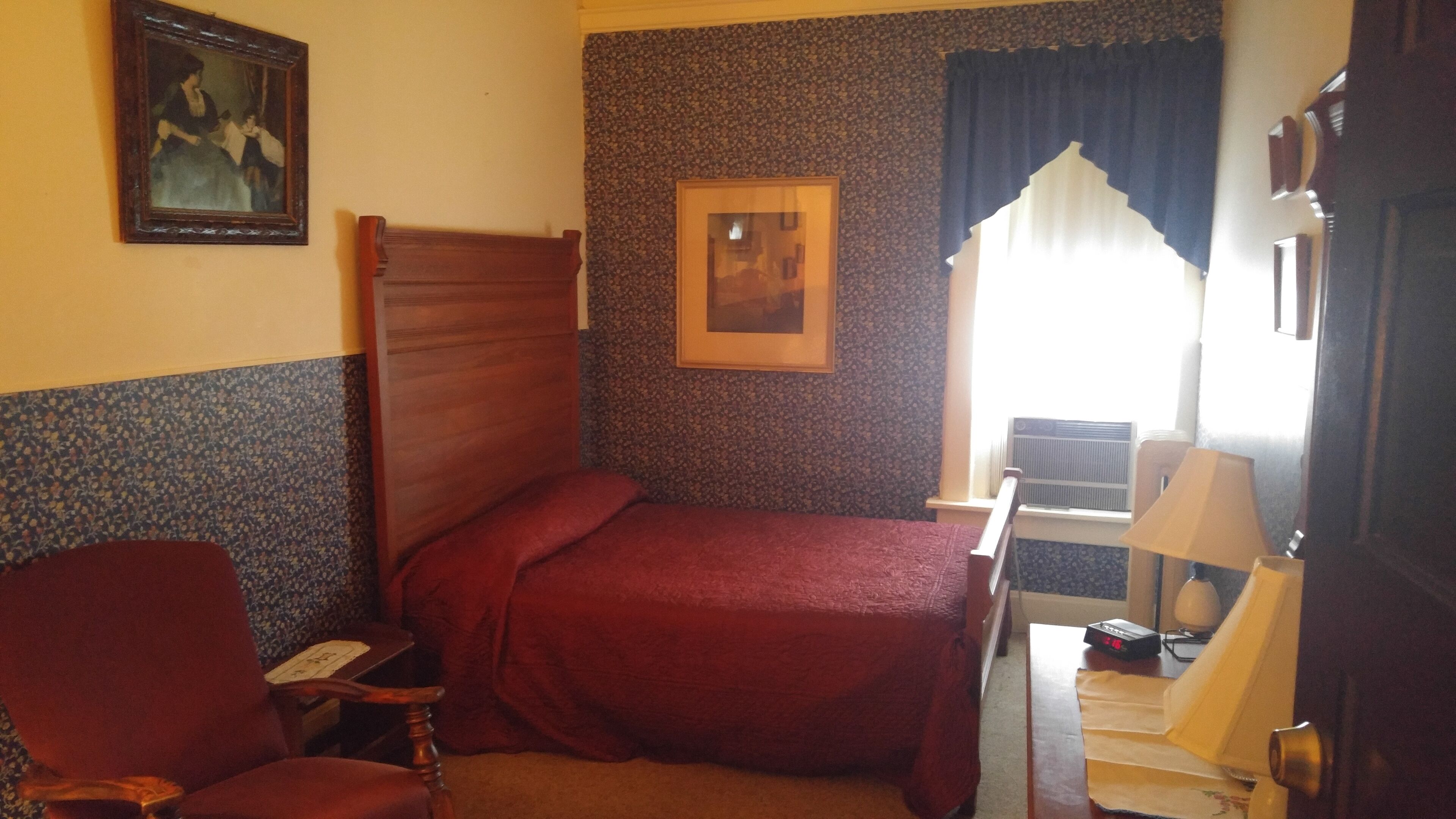 A room with a bed, a chair, a desk, a lamp, and two framed pictures on the wall.