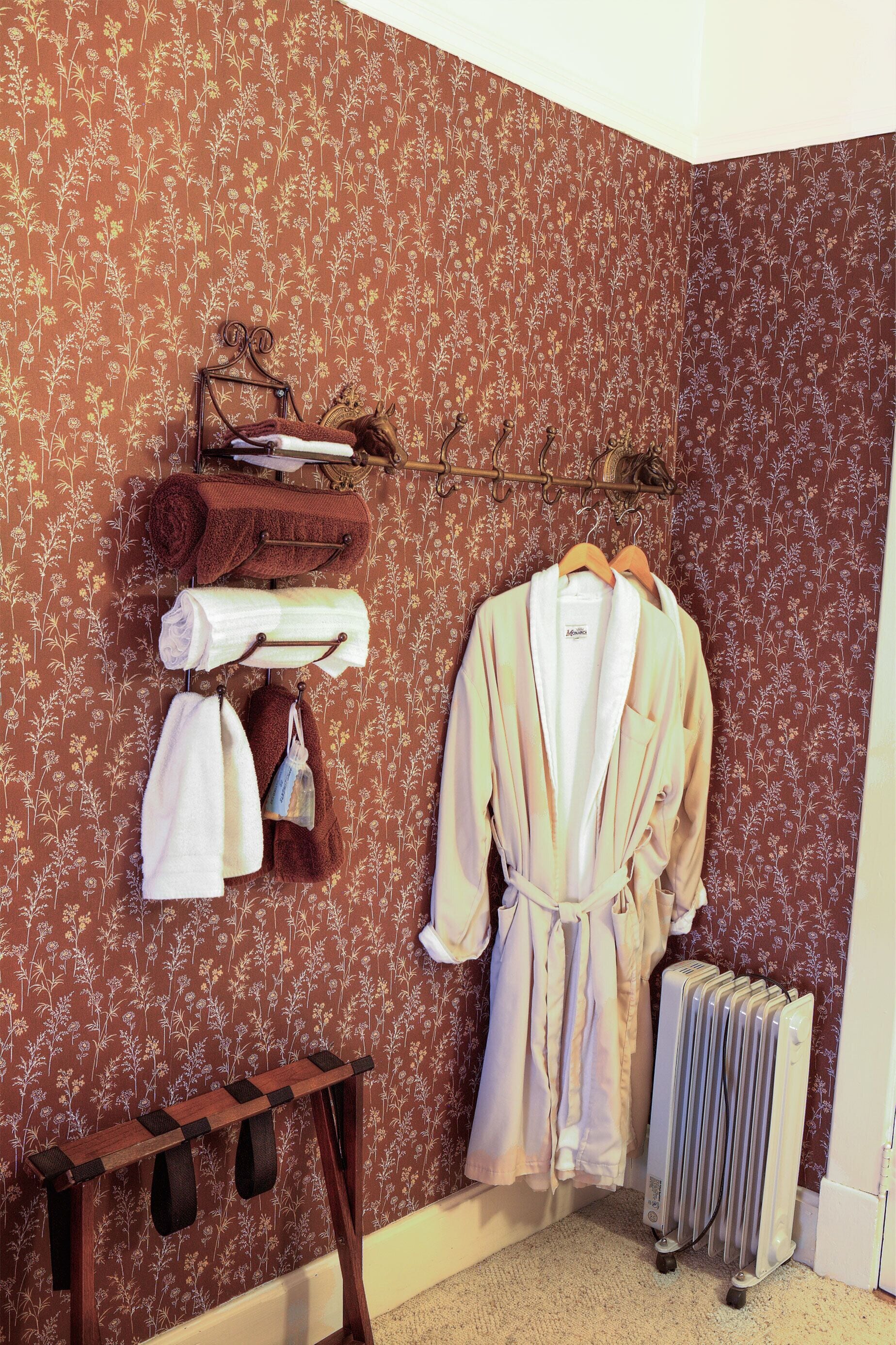 A bathroom with a floral wallpaper, a towel rack with towels, a robe, and a radiator.