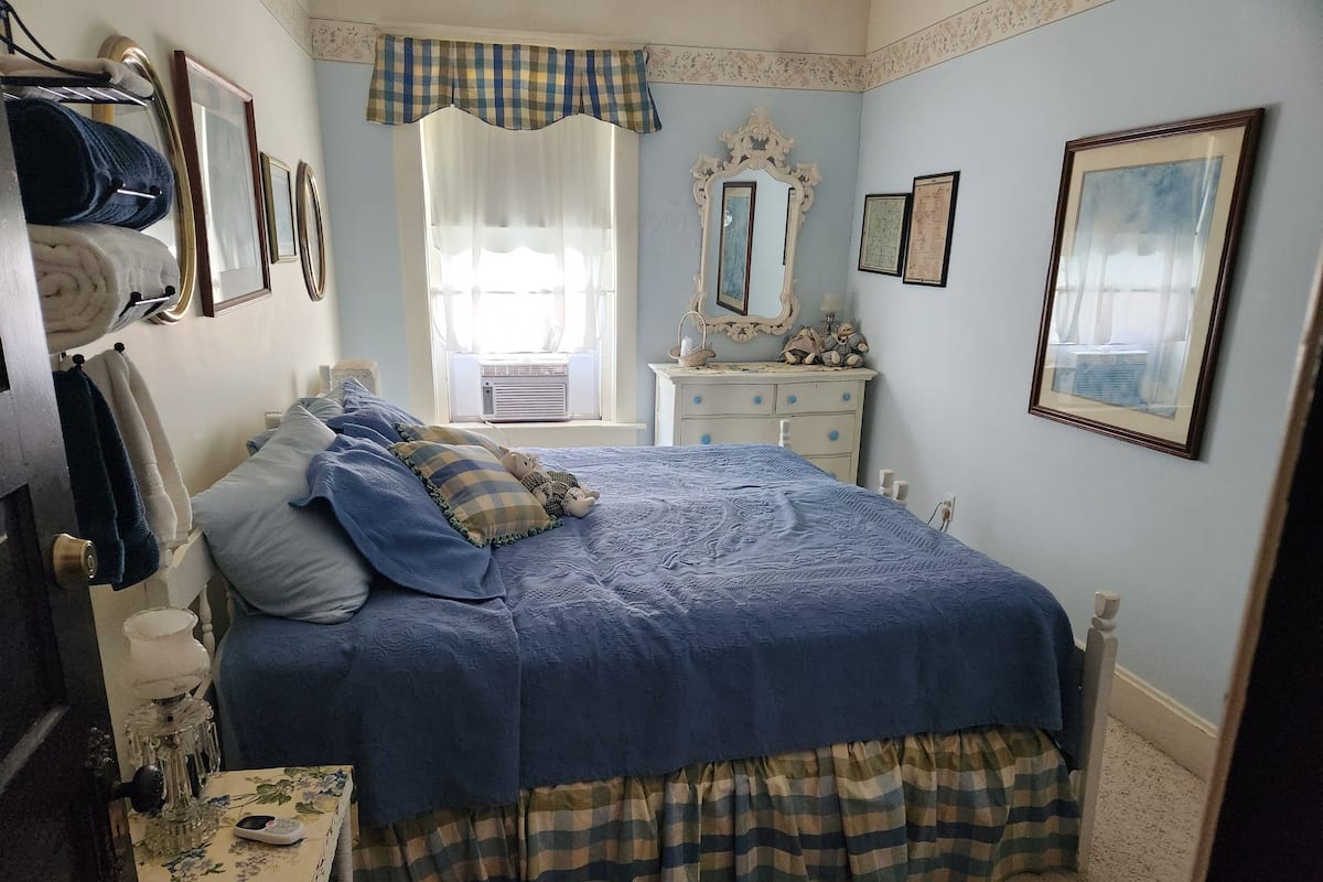A bedroom with a large bed, a dresser, a mirror, and a window with curtains.