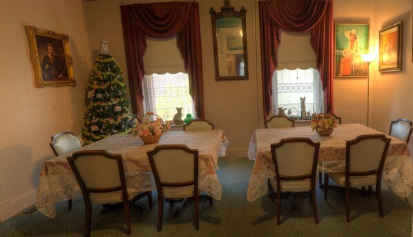 Un comedor con dos mesas, sillas, un árbol de Navidad y un cuadro en la pared.