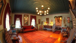A spacious living room with a large red rug, wooden furniture, and a chandelier.