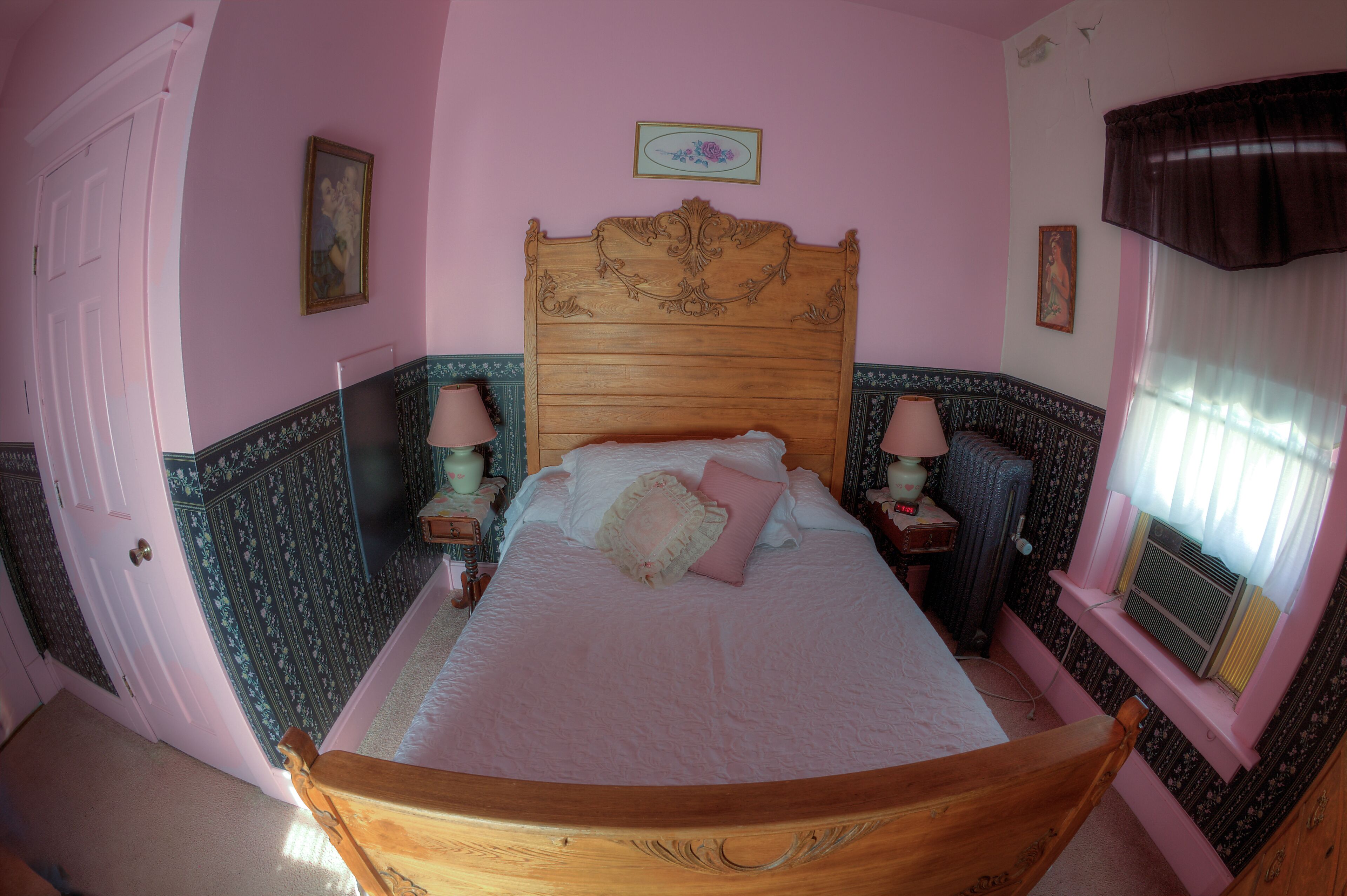 Une chambre avec un lit en bois, deux lampes de chevet, un radiateur et une fenêtre avec des rideaux.