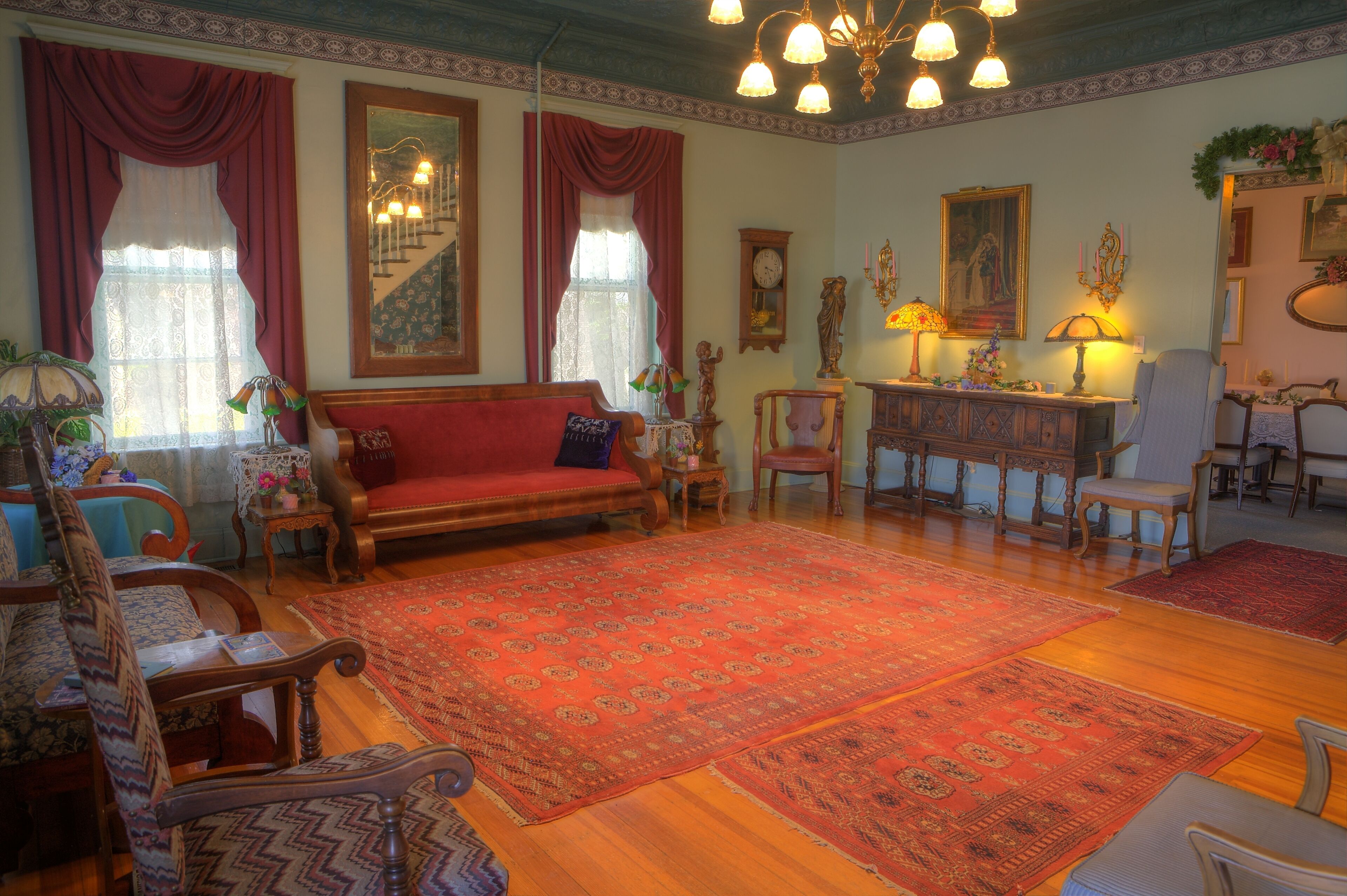 A traditional living room with a red sofa, patterned rugs, wooden furniture, and a staircase with a decorative railing.