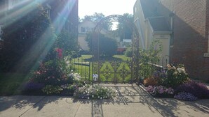 A residential garden with a metal gate, various flowering plants, and a lawn.