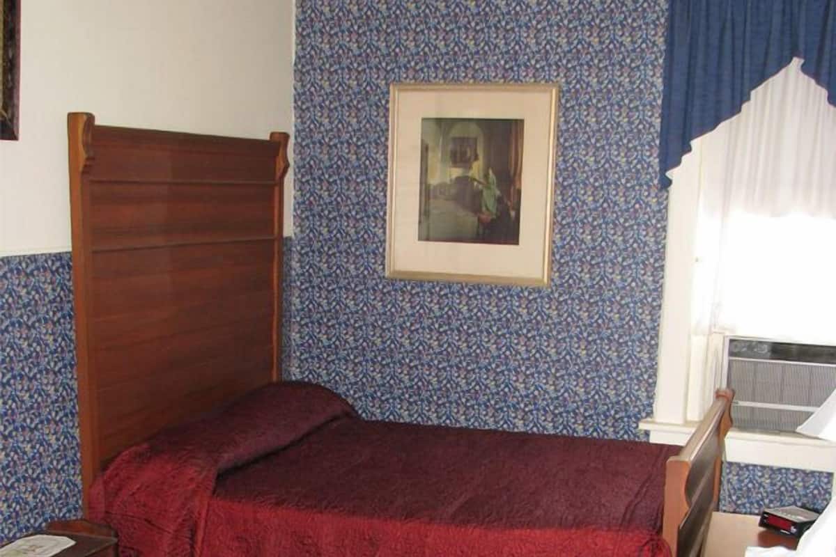 A bedroom with a wooden bed, a framed picture on the wall, a window with blue curtains, and a wooden dresser.