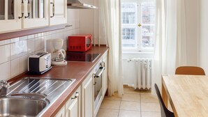 Cocina compacta con lavamanos, estufa y un microondas rojo. Se ve una ventana con cortinas y vistas a edificios.