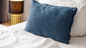 Una cama bien hecha con sábanas blancas y una almohada azul.