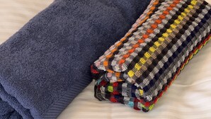 Una cama con una colcha a rayas y una toalla azul doblada.
