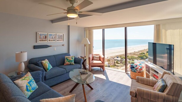 A modern living room with a sofa, armchairs, a coffee table, and a TV. There is a large window with a view of the beach. - Whoa!  Amazing view!! (Myrtle Beach)