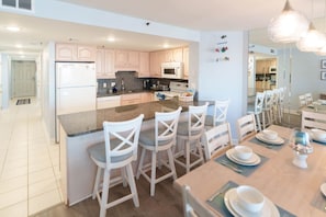 A modern kitchen with a central island, bar stools, and a dining table set for six. - Whoa! Amazing view!! (Myrtle Beach)
