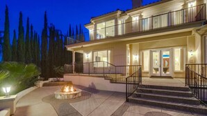 A two-story house with a fire pit in the courtyard, a balcony, and a well-lit entrance.