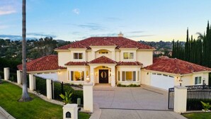 A large, two-story house with a red-tiled roof, a front driveway, and a well-maintained lawn.