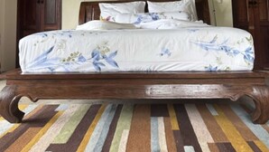 Una cama con dosel, cabecero de madera y una alfombra a rayas multicolores.