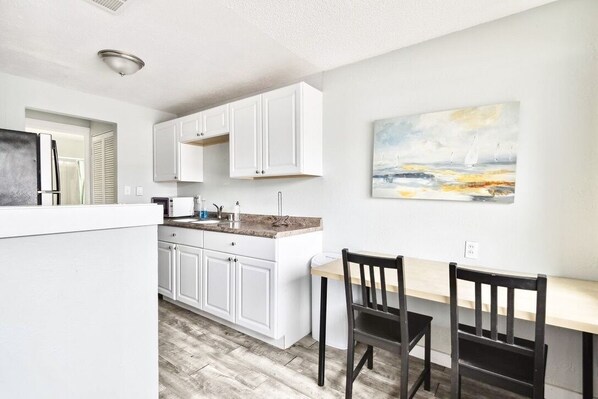 A compact kitchen with white cabinets, a wooden dining table, and a painting on the wall.