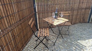 Een houten tafel met metalen poten, een fles en een glas op een grindoppervlak, omringd door een houten hek.