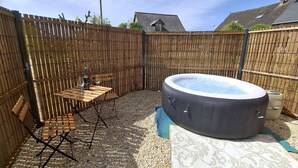 A hot tub in a backyard with a wooden fence, a table with chairs, and a small window. - Le Houx Blanc: Stylish 3 star apartment with pool, private jacuzzi and terrace (Mantilly)