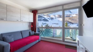 Quarto moderno com sofá cinza, carpete vermelho e uma janela grande com vista para montanhas cobertas de neve.