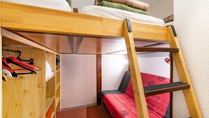 Quarto com beliche, escada de madeira, prateleira com roupas e colcha vermelha e preta.