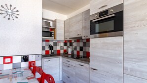 Uma cozinha compacta com eletrodomésticos modernos, uma área de refeições com uma cadeira vermelha e um relógio de parede único.