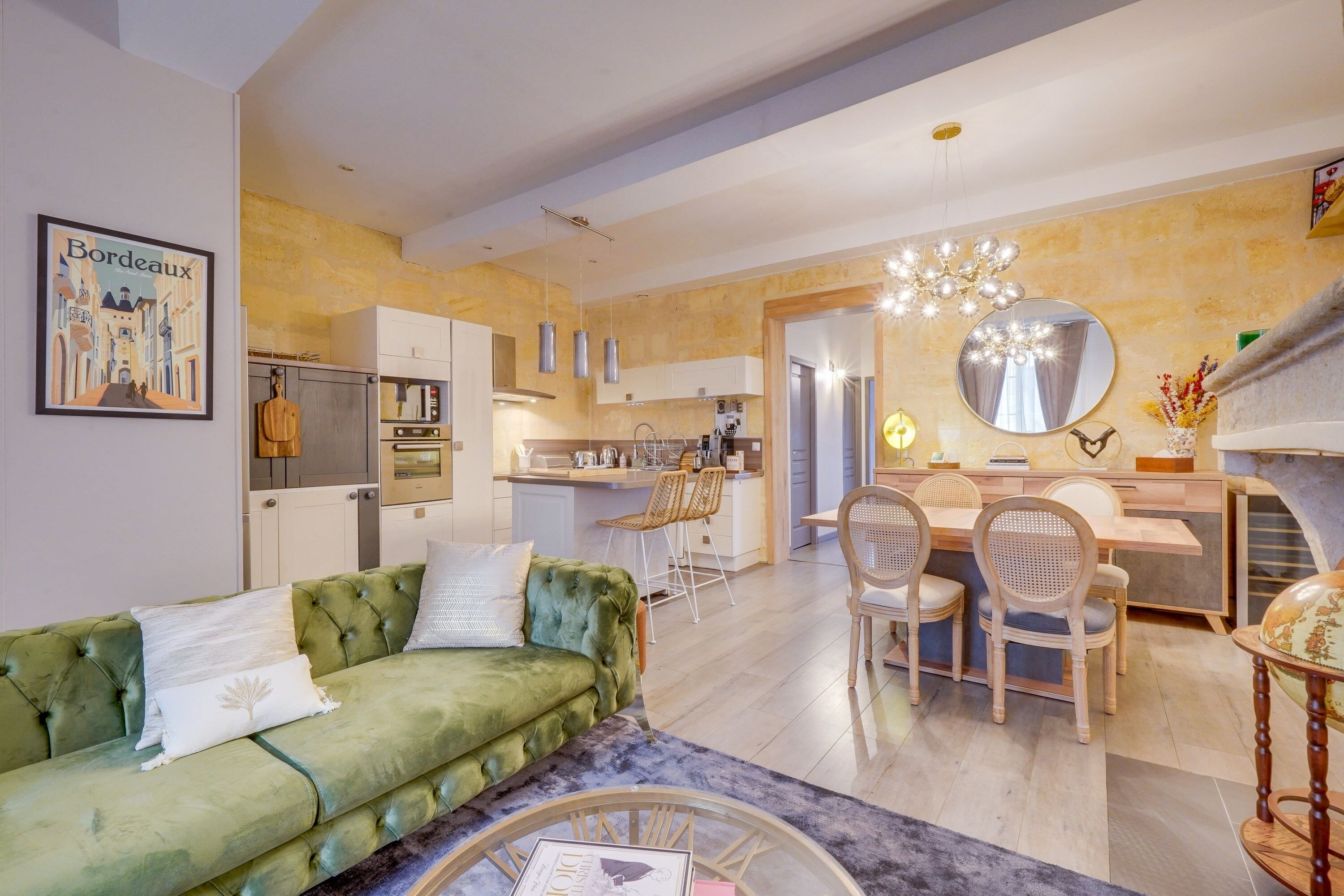 Una sala de estar moderna con un sofá verde, un comedor con sillas de mimbre y una cocina al fondo.