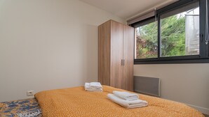 A bedroom with a bed, a wardrobe, and a window with a view of greenery.