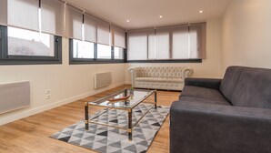 A modern living room with a glass coffee table, a grey sofa, and a beige sofa.