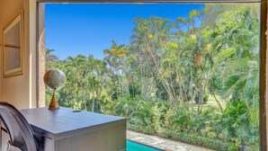 A room with a desk, a globe, and a view of a swimming pool surrounded by lush greenery.