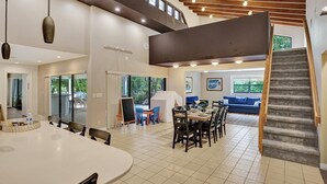 A spacious indoor area with a high ceiling, a dining area with a round table, and a staircase leading to an upper level.