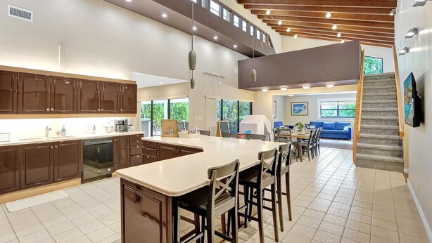 A spacious kitchen with a large island, dark wooden cabinets, and a high ceiling with exposed beams.