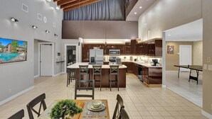 A modern kitchen with a central island, wooden ceiling beams, and a dining area with a view of a swimming pool.
