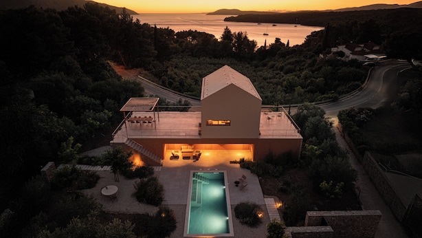 Una casa moderna con piscina, rodeada de árboles y vista al mar al atardecer.