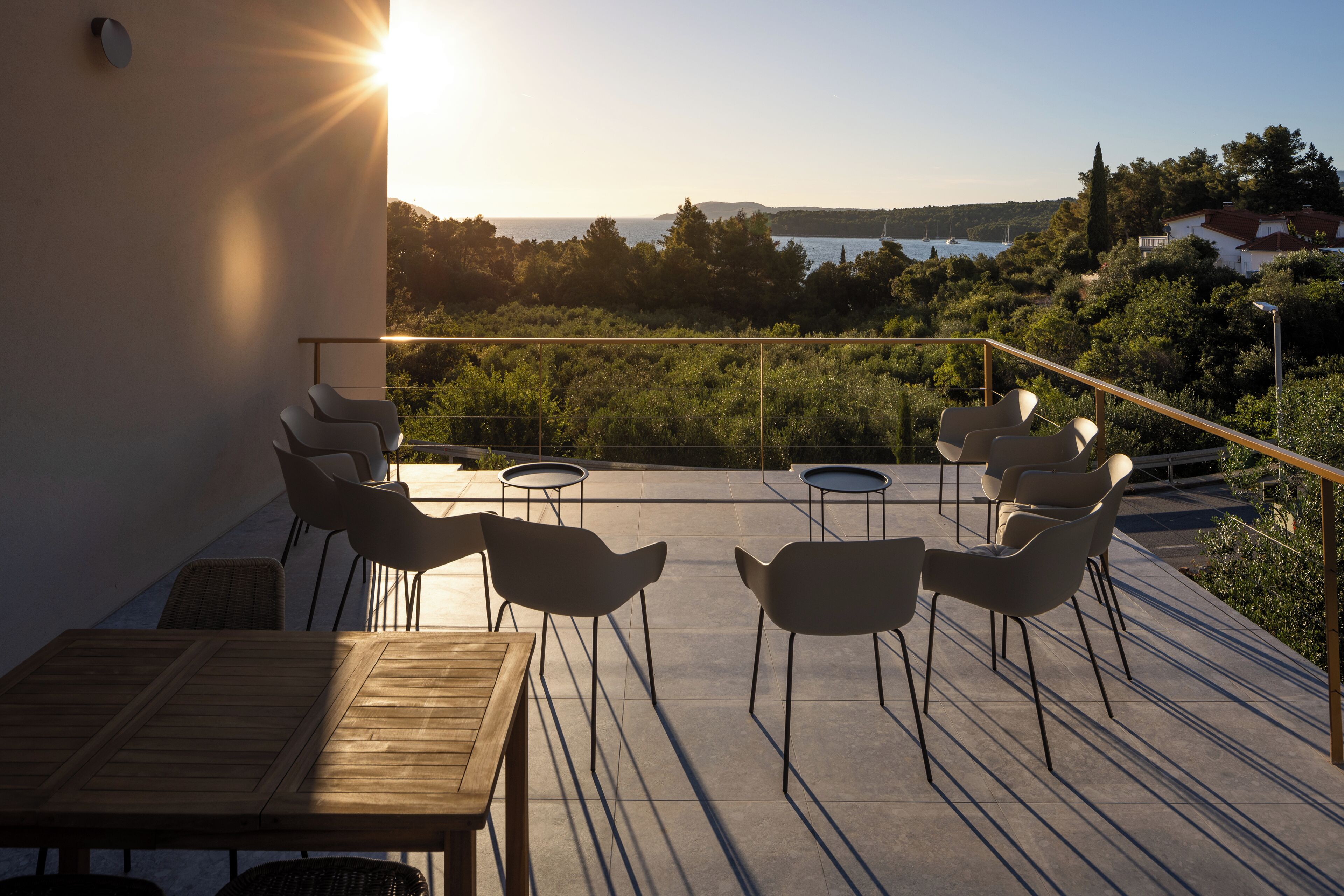 An outdoor seating area with a wooden table and chairs, overlooking a scenic view of a lake and hills.