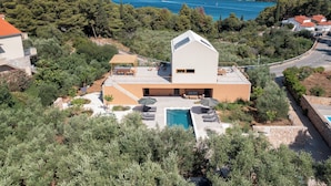 Una villa moderna con piscina, rodeada de exuberante vegetación y vistas al mar.