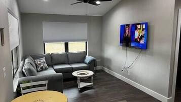 A modern living room with a gray sofa, a small round table, and a ceiling fan.