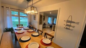 Un comedor con una larga mesa de madera dispuesta para seis personas, una lámpara colgante y vistas al exterior a través de grandes ventanales.