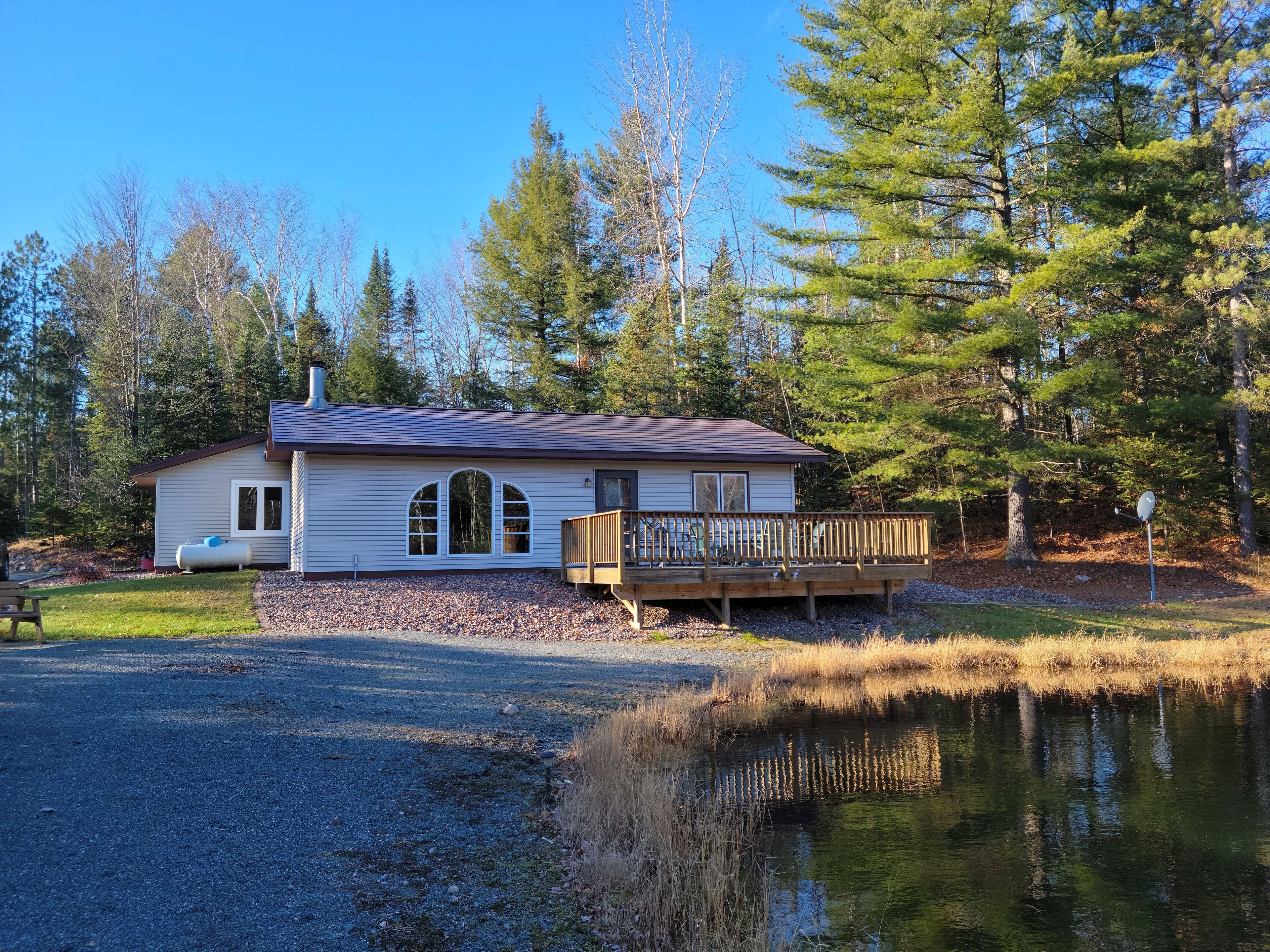 A cabin with a deck, a pond, and a forested area.