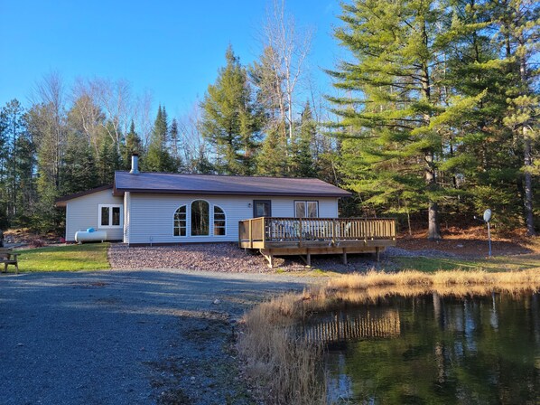 A cabin with a deck, a pond, and a forested area.