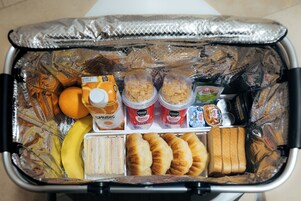 Uma mala cheia de comida, incluindo sanduíches, croissants, bananas e caixas de suco.
