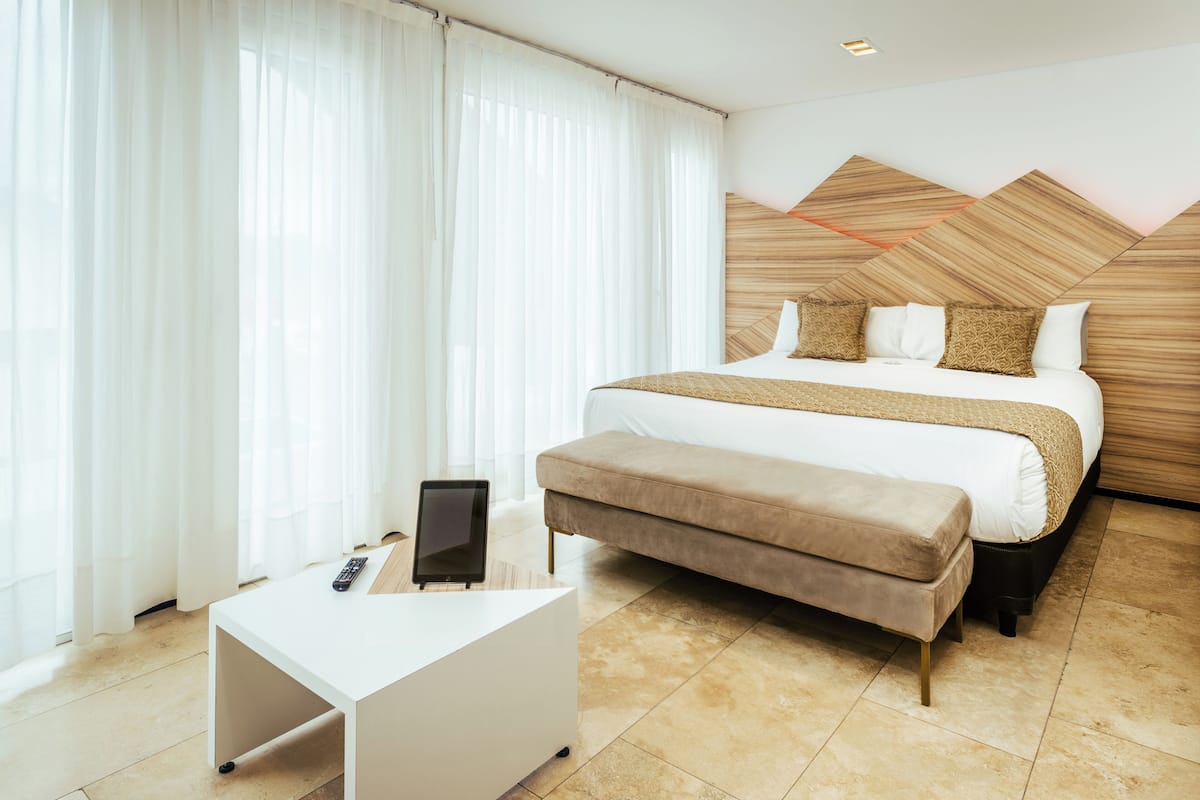 Quarto de hotel moderno com uma cama grande, uma mesinha de cabeceira, um controle remoto e um banco.