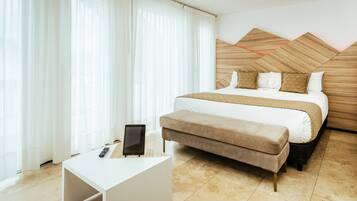 A modern hotel room with a large bed, a bedside table, a remote control, and a bench.