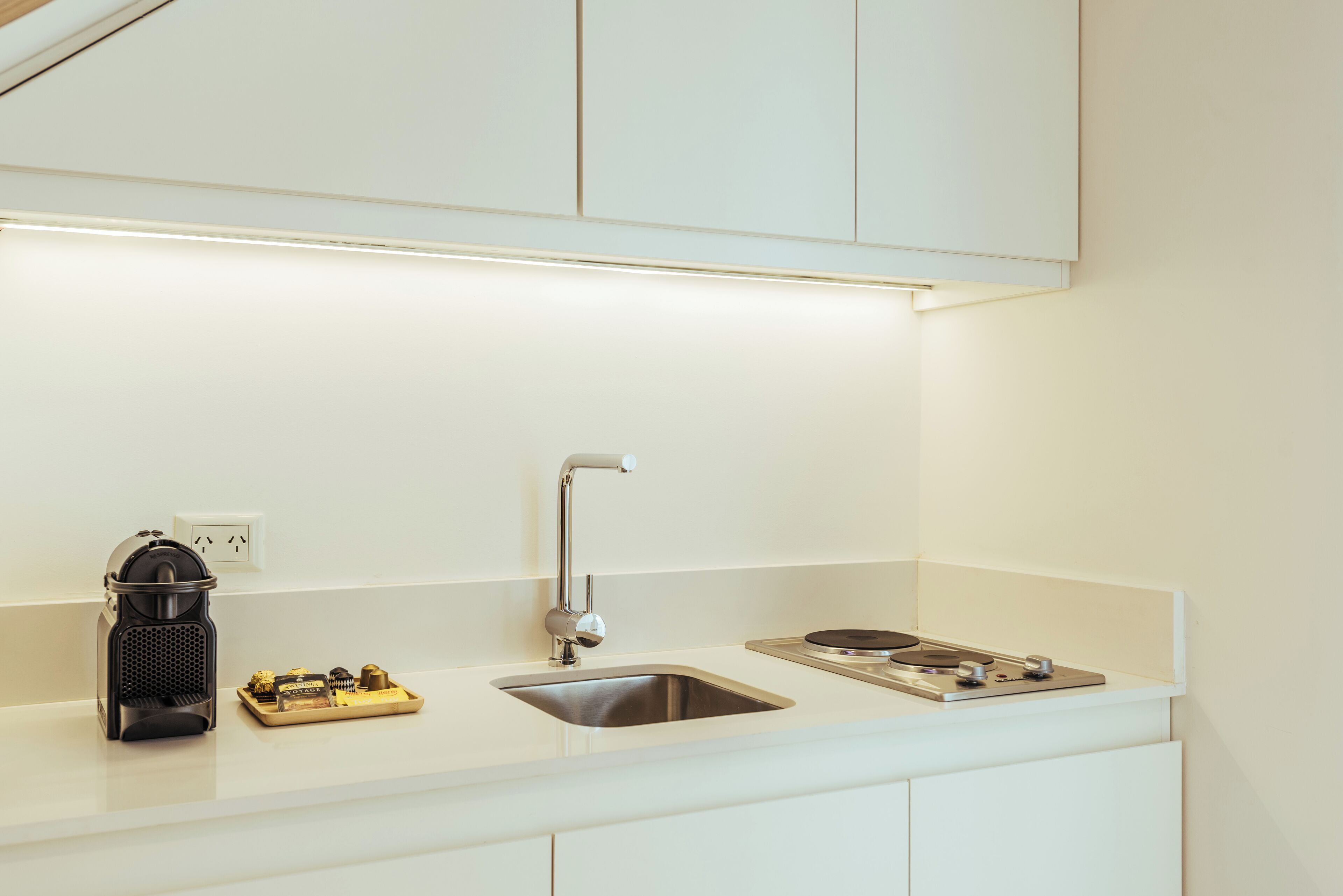 A modern kitchen with a stainless steel sink, a kettle, and a small electric stove.