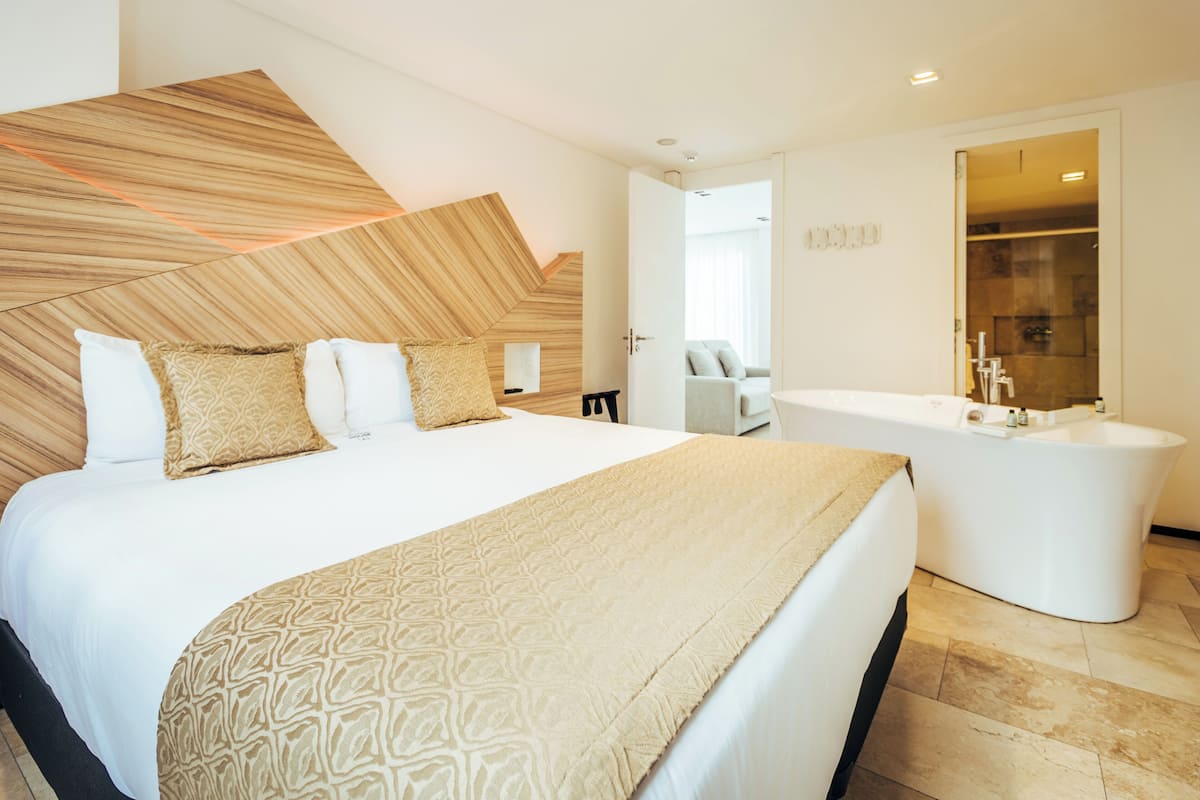 Quarto de hotel moderno com uma cama grande, banheiro separado e vista para a cidade.