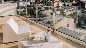 A rooftop terrace with a table set for two, a bottle of champagne, and bowls of snacks.