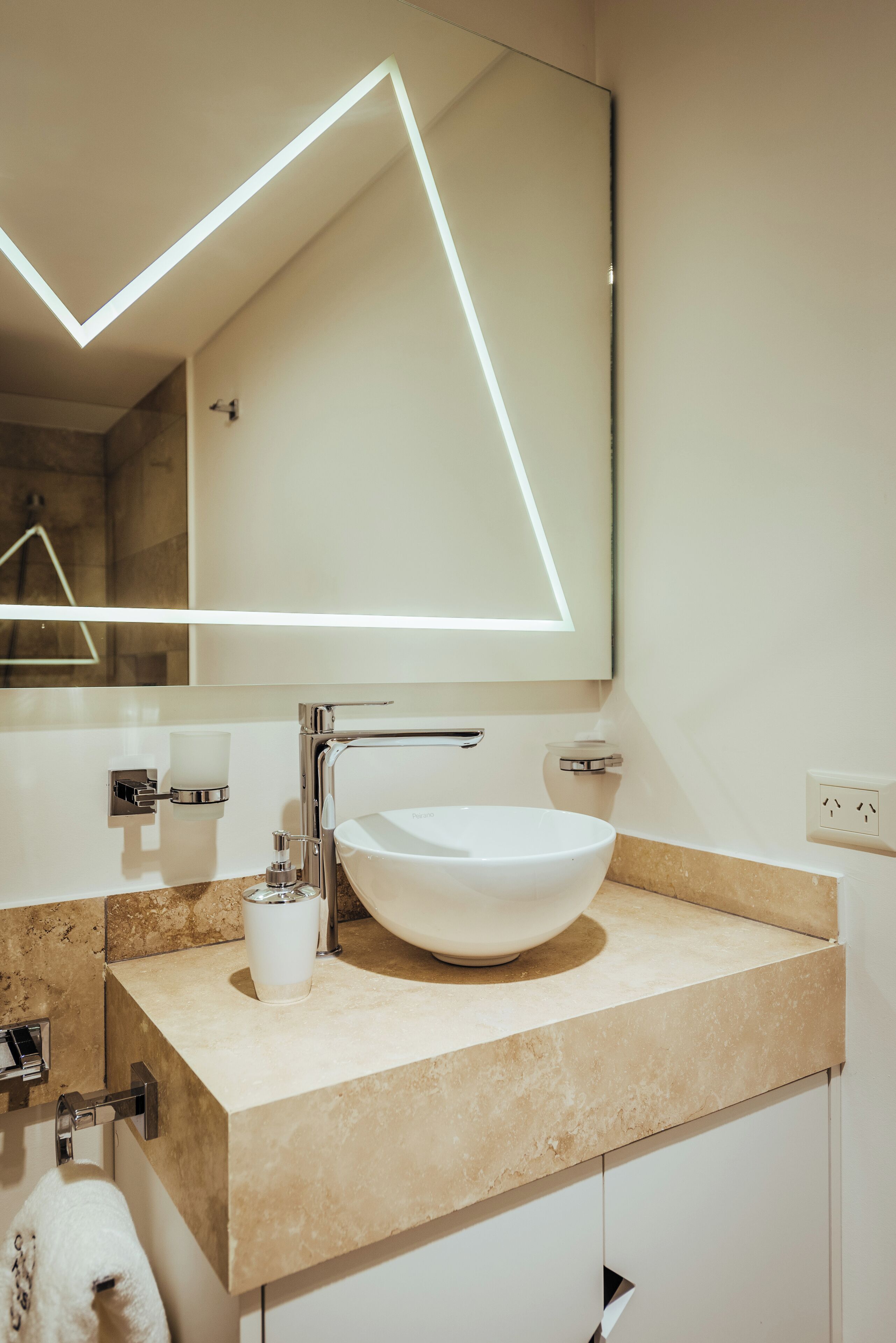 A modern bathroom with a white sink, a mirror with geometric lighting, and a towel rack.