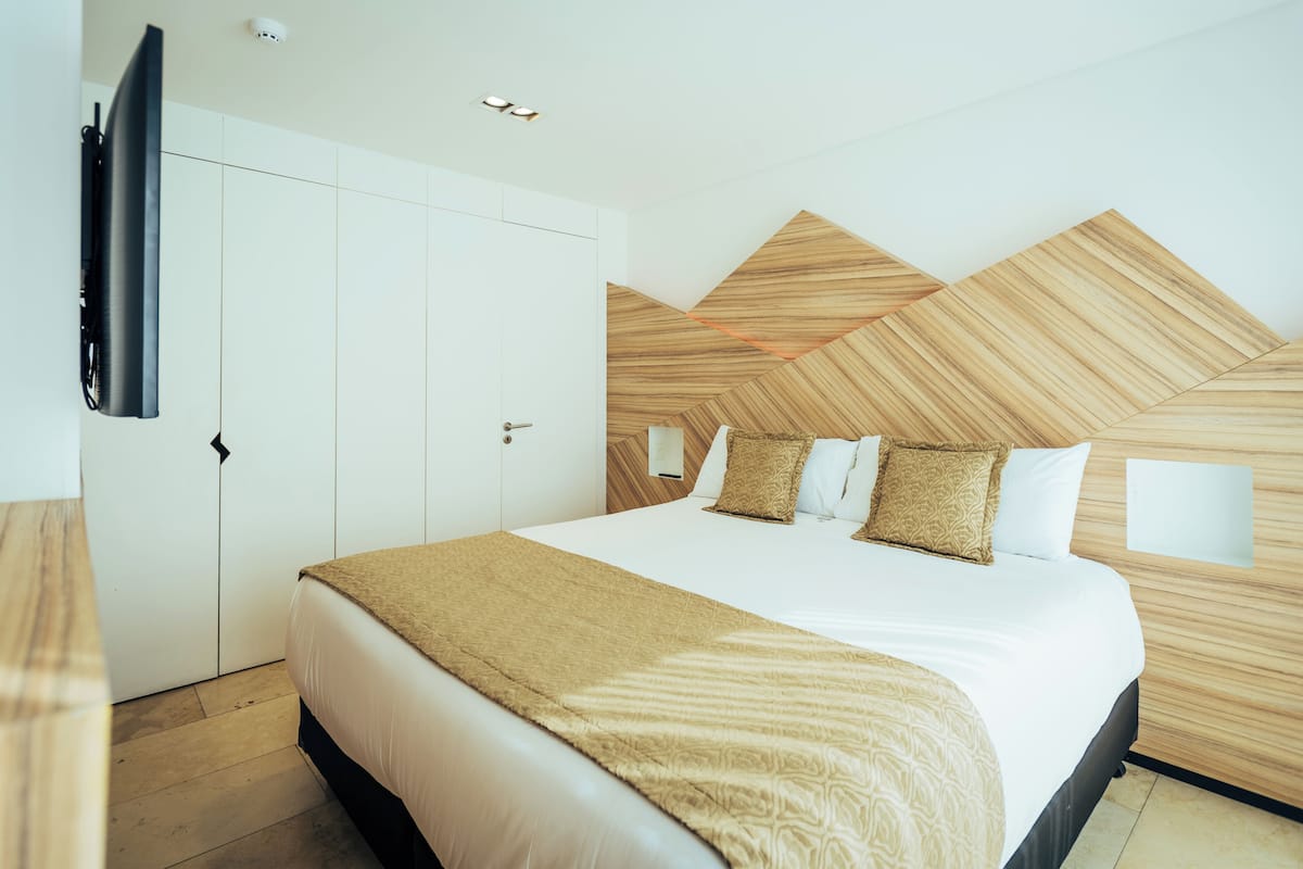 Quarto moderno com uma cama grande, guarda-roupa e TV na parede.